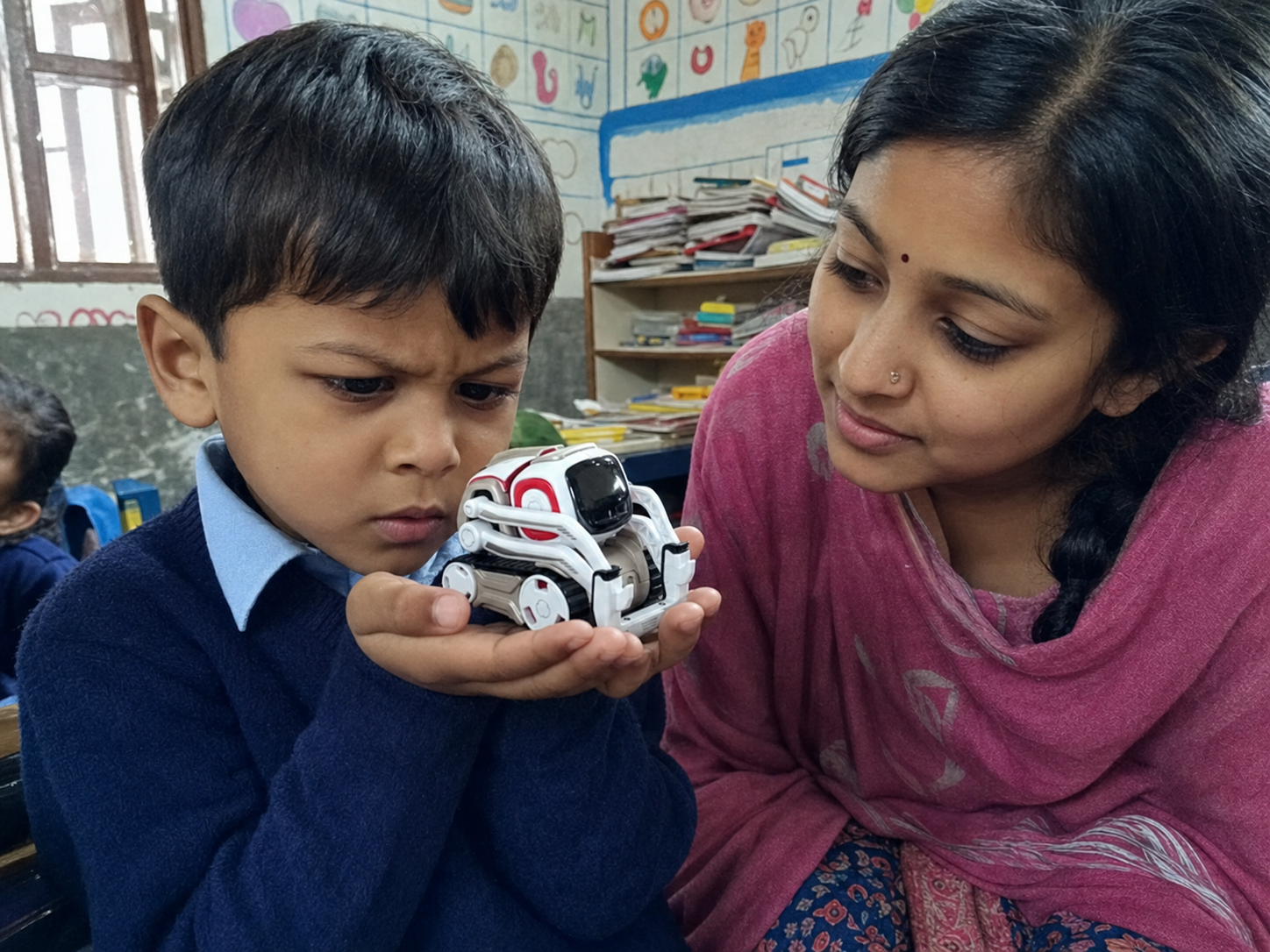 A young boy cradles the tiny robot in his cupped hands, peering at it with a puzzled expression while a teacher watches