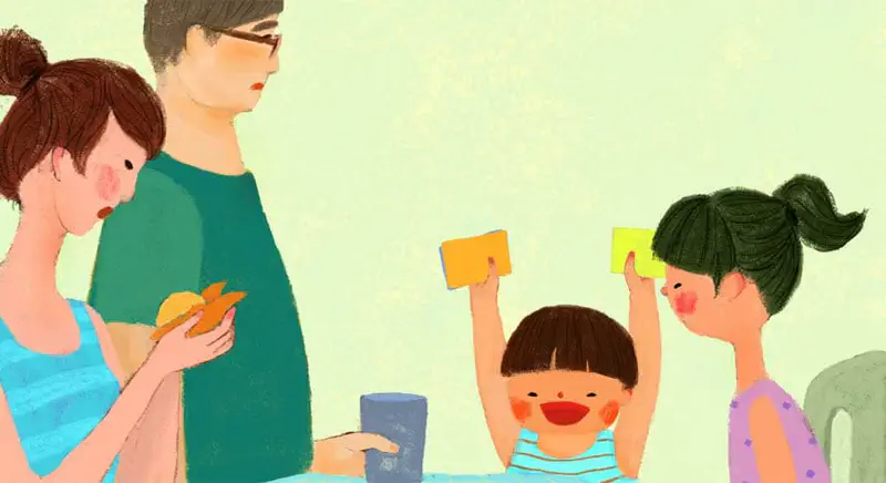 Family at table with mum, dad in glasses, sister, and happy boy holding colored cards
