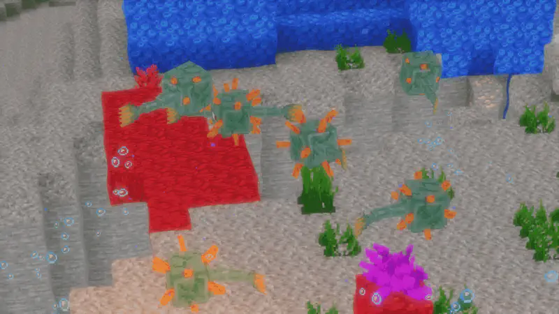 Minecraft underwater scene with drowned zombies walking on sandy ocean floor near red coral, seagrass, and bubbles.