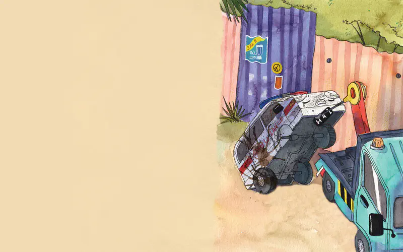 A damaged ambulance with a sad expression sits tilted on a dusty road near a tow truck and colorful corrugated metal buildings.