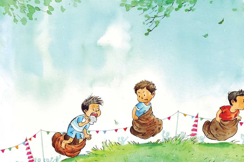 Three boys compete in a sack race hopping across green grass with colorful festival bunting in the background under a blue sky.
