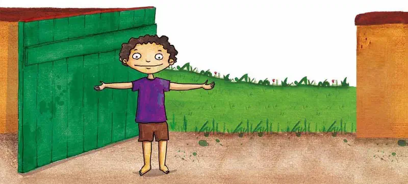 A boy in a purple shirt stands proudly with arms outstretched in front of a green painted gate. Yellow wall and grass behind him.