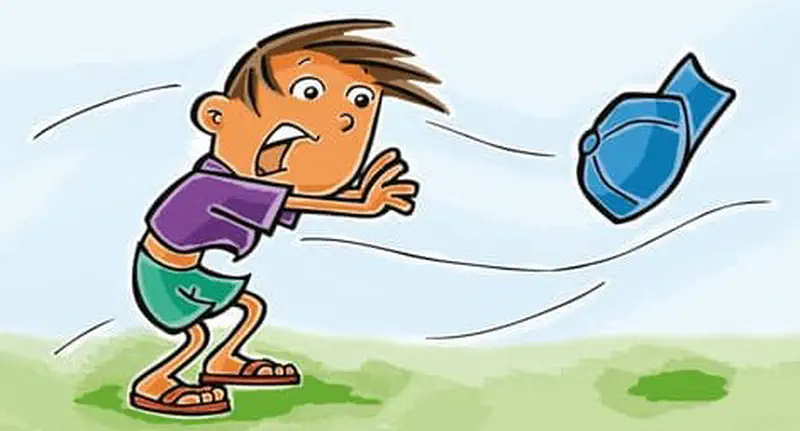 A frustrated boy chases after his blue cap as it blows away in the wind across a grassy field.