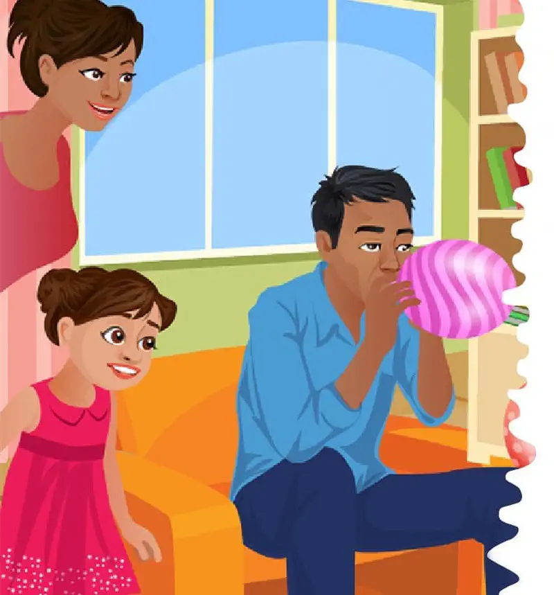 A father blows up a pink striped balloon while sitting on an orange couch as mom and daughter watch nearby.