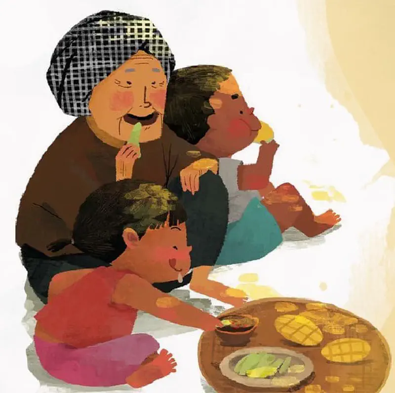 A grandmother in a headscarf and two children sit together eating mangoes and green fruit from a wooden tray with dipping sauce.