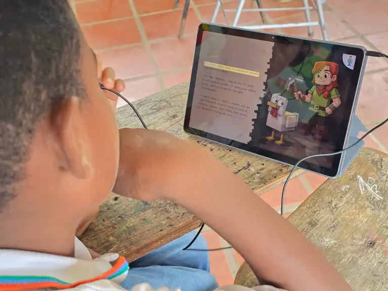 A student at a school in Colombia reads a Spanish story in the Bookbot app during the pre-pilot. The sentence being read is highlighted in yellow, beside an illustration of a girl and a blocky white chicken.